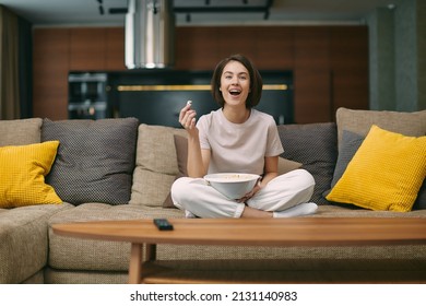 Laughing Happy Pretty Young Girl Watching Sitcom Movie Or Stand Up Comedy, Sitting On Sofa With Popcorn, Rest At Home