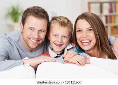 Laughing happy young family posing together in the living room with an adorable young boy with missing front teeth flanked by his attractive smiling parents