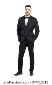 Laughing Happy Young Man In Tuxedo With Bow Tie Looking At Camera. Full Body Length Portrait Isolated Over White Studio Background.