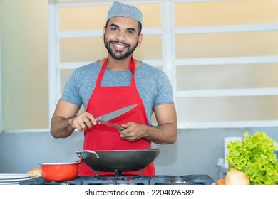 Laughing Hispanic Cook With Red Apron Preparing Food At Kitchen Of Restaurant