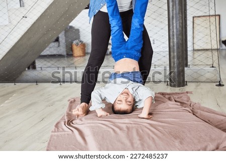 Laughing kid having fun doing handstand upside down with mother support at home