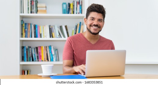 Laughing Latin American Man With Beard Working At Computer At Home