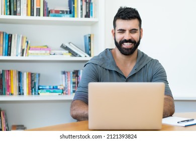 Laughing Latin American Man With Hipster Beard At Computer At Office