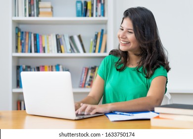 Laughing Latin American Young Adult Woman At Computer At Desk At Home