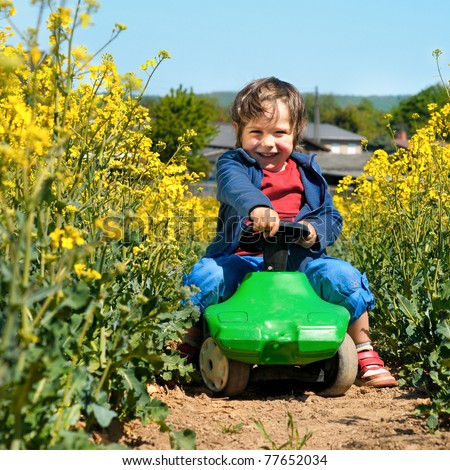 Laughing little boy drives toy car via rapeseed field in bloom