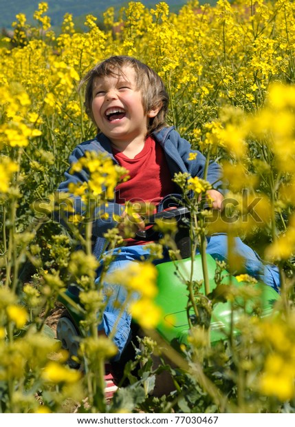 Laughing little boy drives toy car via rapeseed\
field in bloom