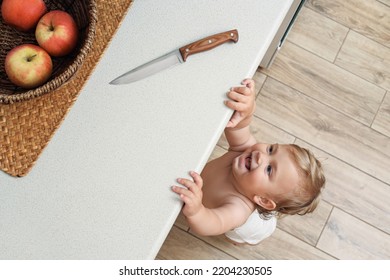 Laughing Little Child Reaching For Knife On Light Countertop, Above View. Dangers In Kitchen