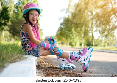 Laughing loudly, a funny girl with Afro-pigtails and wearing sports protective gloves and a helmet sat down to rest on the sidewalk after roller skating. A child's favorite hobby is roller skates.