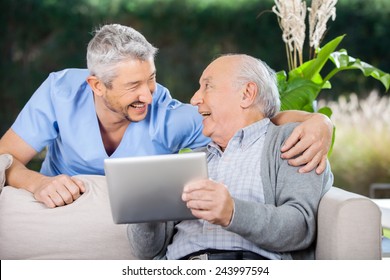 Laughing male caretaker and senior man using tablet computer at nursing home porch