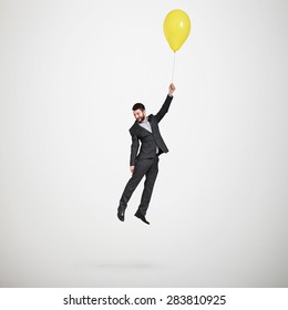 laughing man flying with yellow balloon and looking down over light grey background  - Shutterstock ID 283810925