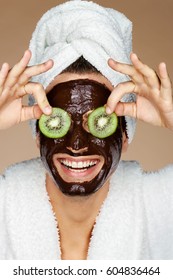 Laughing man receiving spa treatments. Photo of young man with pieces of kiwi in his eyes and chocolate face mask. Beauty & Skin care concept