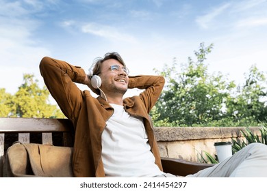 Laughing man sitting on bench listening music with headphones - Powered by Shutterstock