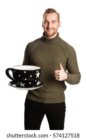 Laughing Man Wearing A Green Turtle Neck Sweater And Holding A Big Oversized Mug. Standing Against A White Background.