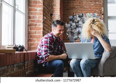 Laughing man and a woman with a laptop sitting in an armchair by the window. Couple in modern loft interior. - Shutterstock ID 1177672987