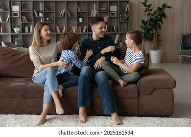 Laughing married couple tickling little adorable son and daughter, playing together seated on soft sofa in cozy living room. Family value and love, funny leisure activity with children at home concept