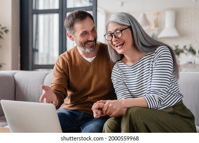 Laughing Mature Couple Parents Watching Fun Movie Together, Having Video Call On Laptop Talking With Relatives, Children, Friends. Middle-aged Wife And Husband Communicating Online.