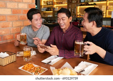 Laughing mature friends drinking beer and watching videos on smartphone - Powered by Shutterstock