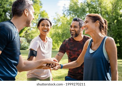 Laughing mature and multiethnic sports people at park. Happy group of men and women smiling and stacking hands outdoor after fitness training. Mature sweaty team cheering after intense training. - Shutterstock ID 1999270211