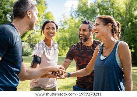 Laughing mature and multiethnic sports people at park. Happy group of men and women smiling and stacking hands outdoor after fitness training. Mature sweaty team cheering after intense training.