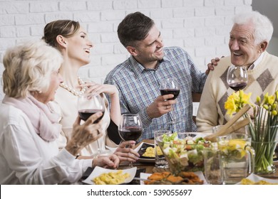 Laughing Members Of The Family Holding Glasses Of Wine During Dinner