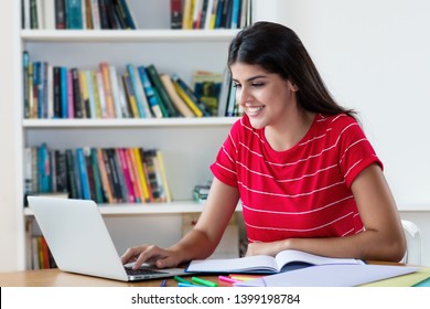 Laughing mexican female student learning on computer indoors at desk