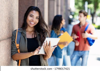 Laughing mexican student with tablet computer and friends in background in front of university building outdoor in summer in city - Powered by Shutterstock