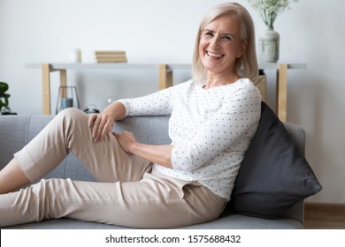 Laughing Middle-aged Woman Leaned On Cushion Sitting On Comfy Couch Resting Feels Happy And Overjoyed Posing Looking At Camera, Enjoy Free Time And Retired Life, Well-being Senior 50s Female Concept