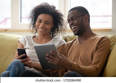 Laughing millennial african american man and woman couple looking at smartphone screen. Smiling and happy husband and wife watching funny online video together in social network. - Powered by Shutterstock