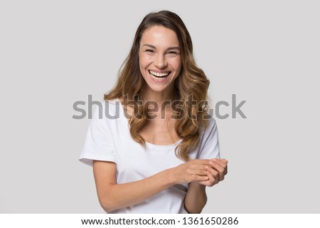 Laughing millennial woman posing over white wall background looking at camera feels overjoyed happy, head shot portrait. Concept of positive news, rejoice facial expressions, having fun and happiness