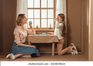 Laughing Mother And Daughter Having Tea Party In Cardboard House