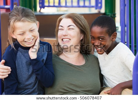 Laughing mother embracing two giggling young sons at park outside