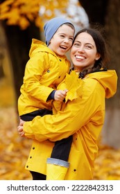 Laughing Mother In Yellow Raincoat With Son Walking And Having Fun In The Autumn Park. Concept Of Happy Family