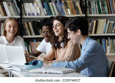 Laughing multi ethnic students use laptop studying or having fun using laptop sit at shared table in university library, having friendly relations, prepare for exams together using modern tech concept