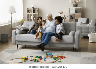 Laughing multigenerational family spend time at home using smartphone, great-grandpa and three cute multiethnic great-grandsons enjoy virtual meeting with relatives, watch cartoons or educational blog - Powered by Shutterstock