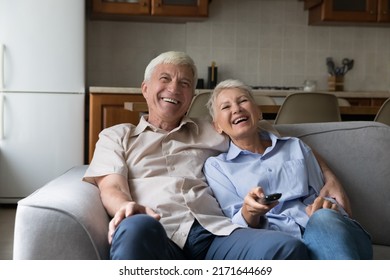 Laughing Older Couple Relax On Sofa Spend Carefree Weekend Together At Home, Hold Remote Control Switch Channels Enjoy Movie, Watch Favourite Funny TV Show Use Online Stream Services. Leisure Concept