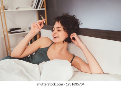 Laughing. Pleased girl laying at the bed and enjoying her lazy day at home at the morning with cannabis cigarette. Funny mood and marijuana concept. Stock photo