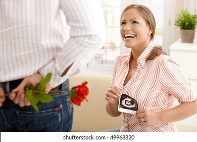 Laughing pregnant woman with ultrasound baby picture in hand getting red rose from man. - Powered by Shutterstock