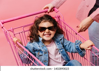 Laughing Preteen Kid Sitting In Shopping Cart. Studio Shot Of Curly Child In Denim Jacket And Sunglasses.