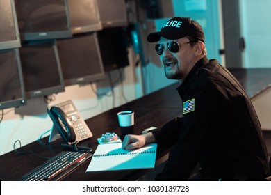 Laughing Prison Guard Sitting At Working Table And Monitoring People In Jail