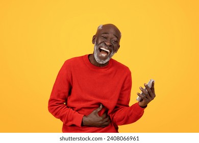 Laughing senior Black man clutching his stomach and holding a smartphone, possibly reacting to funny content, in a red sweater against a yellow background, representing joy and technology use - Powered by Shutterstock