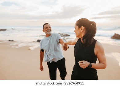 Laughing senior caucasian lady in sportswear leads man by hand, motivate for training and active lifestyle on beach in morning, outdoor. Jogging, relationships, sports together - Powered by Shutterstock