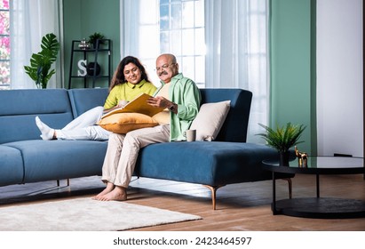 Laughing senior Indian couple sitting on the couch at living room watching photo album - Powered by Shutterstock