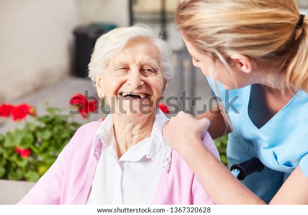 Laughing senior woman and caring geriatric nurse\
together in nursing\
home