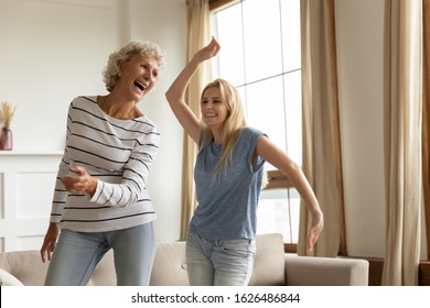 Laughing sincere elderly mature hoary mother having fun with joyful grown up daughter at home. Overjoyed blonde millennial granddaughter dancing to favorite music with happy excited old granny.