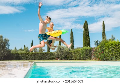 Laughing Son With Father In The Inflatable Ring Having Fun On A Merry Vacation. Cheerful Fooling Around They Jumping To The Swimming Pool. Family Time, Fatherhood, Or Childhood Concept Image.