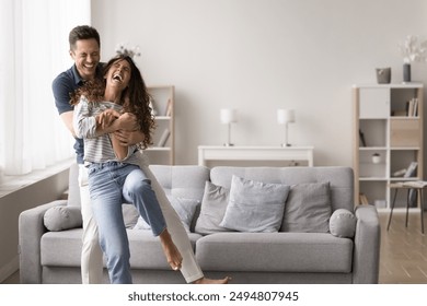 Laughing spouses hugging, dancing, having fun in living room. Playful and affectionate moment between light-hearted couple at home. Partners enjoy their romantic relationship in cozy domestic setting - Powered by Shutterstock