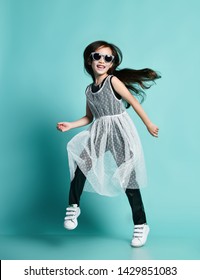 Laughing Stylish Asian Baby Girl Kid In High Fashion Black And White Clothes And Sunglasses Jumps Dances Cool In Gangnam Style At Birthday Party On Blue Mint Background