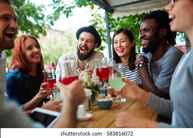 Laughing teenagers with drinks having rest in outdoor cafe