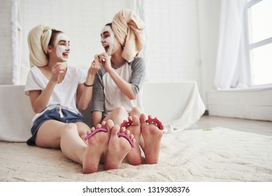 Laughing together. Pedicure and painted leg nails. Conception of skin care by using white mask and cucumbers on the face. - Shutterstock ID 1319308376
