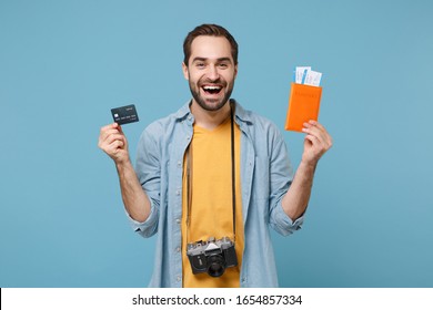 Laughing traveler tourist man in summer clothes with photo camera isolated on blue background. Passenger traveling on weekends. Air flight journey Hold passport boarding pass tickets credit bank card